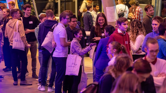 Young women and men in casual clothes stand together in groups and chat.