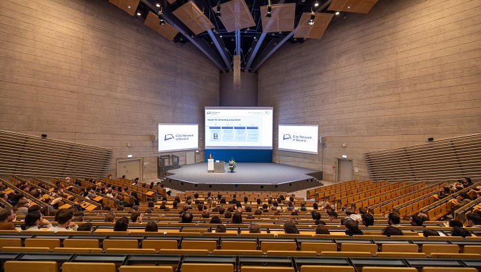 A view from above of the well-filled rows and the stage of the largest lecture hall at TU Munich.