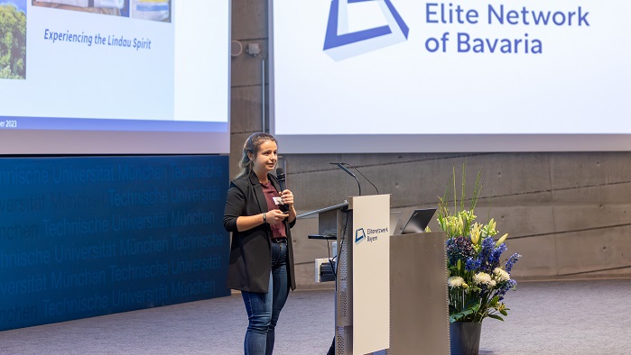 A young woman in jeans and a blazer ist standing on the stage of the lecture hall and speaking to the audience.