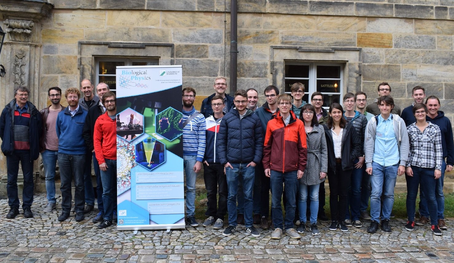 Gruppenbild: Studierende und Lehrende des Elitestudienprogramms „Biological Physics“ vor einem Gebäude.