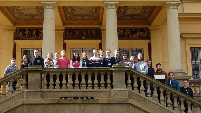 A group of young people stands on a staircase in front of an ancient building.