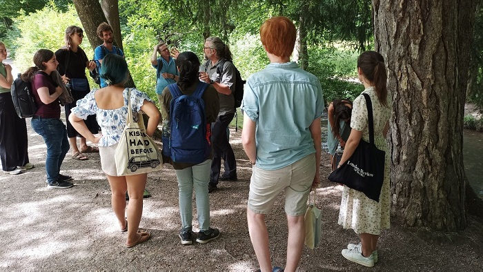 A group of students and Norbert Pantel standing nearby trees in the Augsburg city forest.