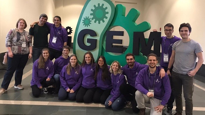 A group of people in purple sweaters in front of the iGEM sign.