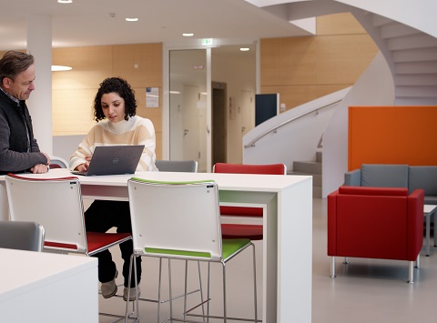 A woman is sitting at a table looking at a laptop.