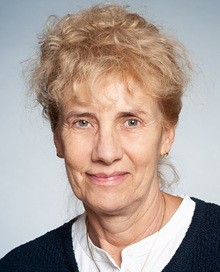 Portrait of a woman with curly blonde hair wearing a white shirt under a dark knitted sweater.