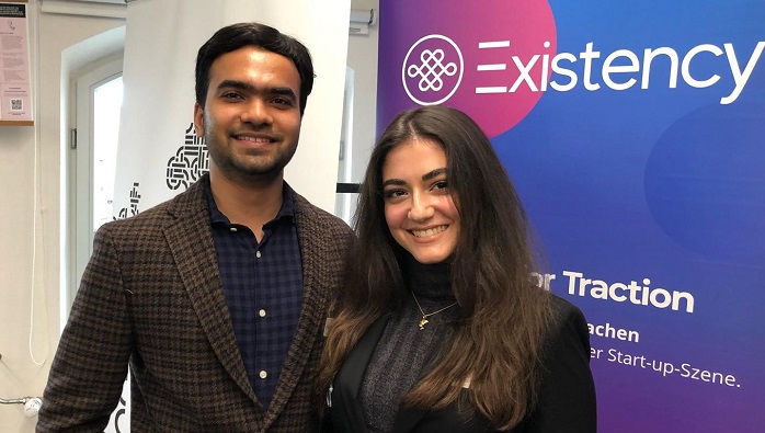 A young man and a young woman in elegant clothes are smiling at the camera.