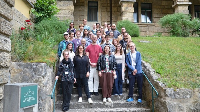 A large group is standing on a staircase in front of a historic building (Wildbad Rothenburg) and posing for a photo.