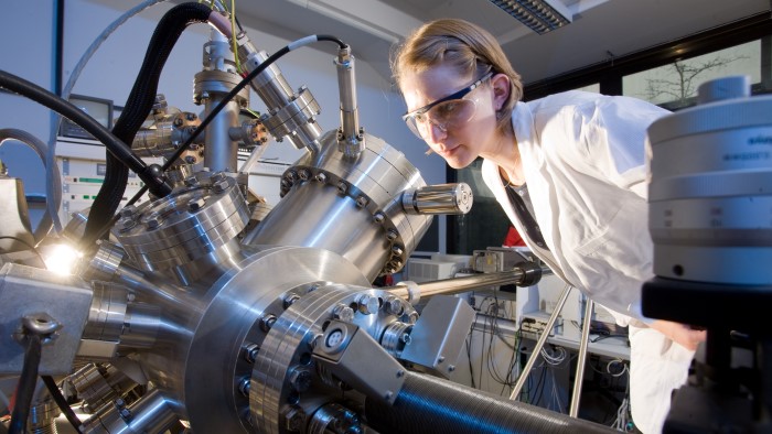 A young woman in a laboratory observes something on an apparatus.