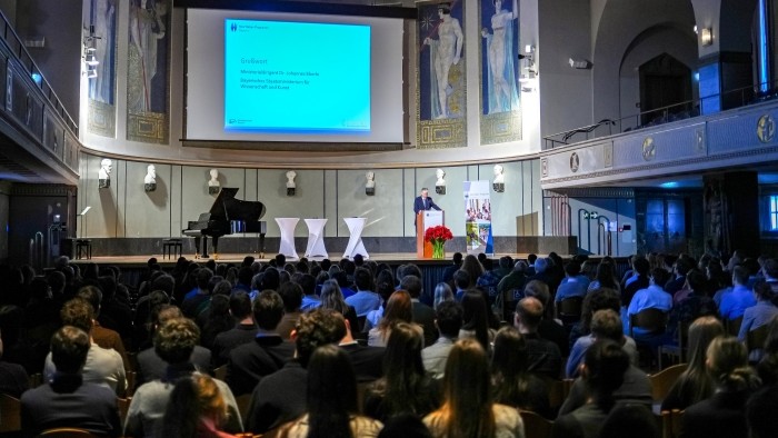 Zuschauer lauschen einer Rede in einer großen festlichen Aula.