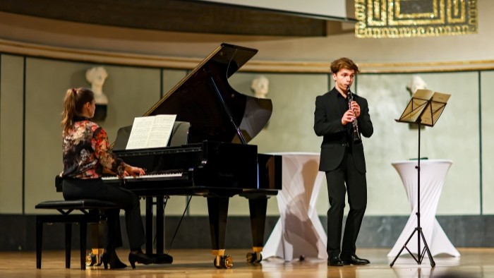 Auf einer Bühne spielen eine Person am Flügel und eine zweite Klarinette.