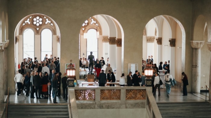 Im Foyer der LMU München stehen zahlreiche Gäste in kleinen Gruppen beisammen und unterhalten sich, umgeben von hohen Bögen und viel Tageslicht.