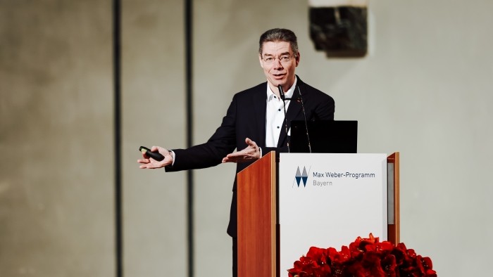 Eine Person hält eine Ansprache am Rednerpult mit der Aufschrift Max Weber Programm Bayern.