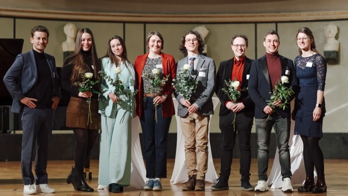 8 Personen stehen auf einer Bühne und posieren für ein Gruppenbild.