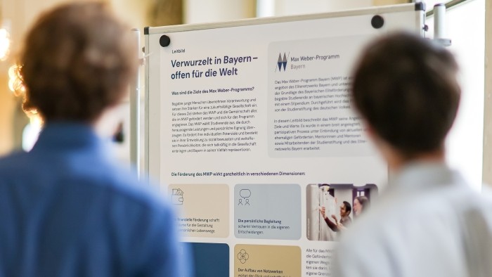 Zwei Personen stehen vor einer Stellwand mit dem Leitbild des Max Weber-Programms.