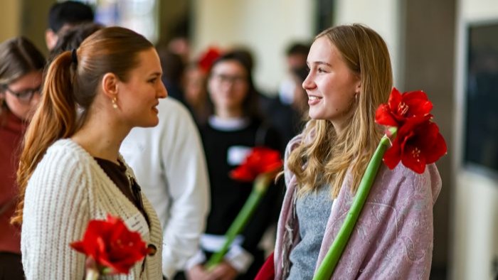 Zwei Gäste im lebhaften Gespräch, jede mit einer leuchtend roten Blume in der Hand.