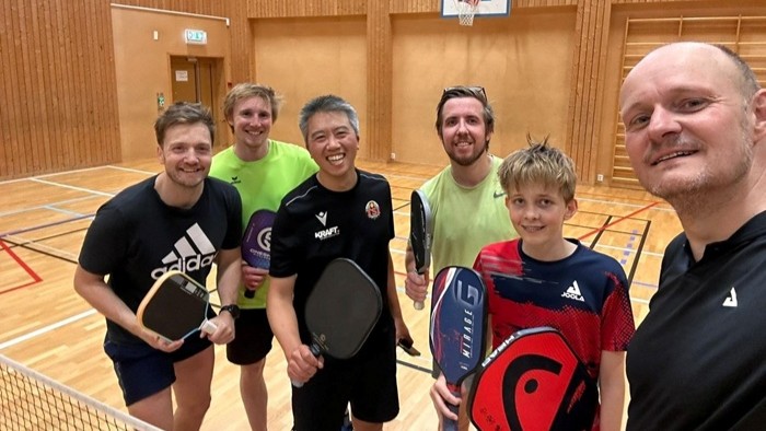Eine Gruppe von Personen steht in einer Sporthalle und hält Pickleball-Schläger in der Hand.