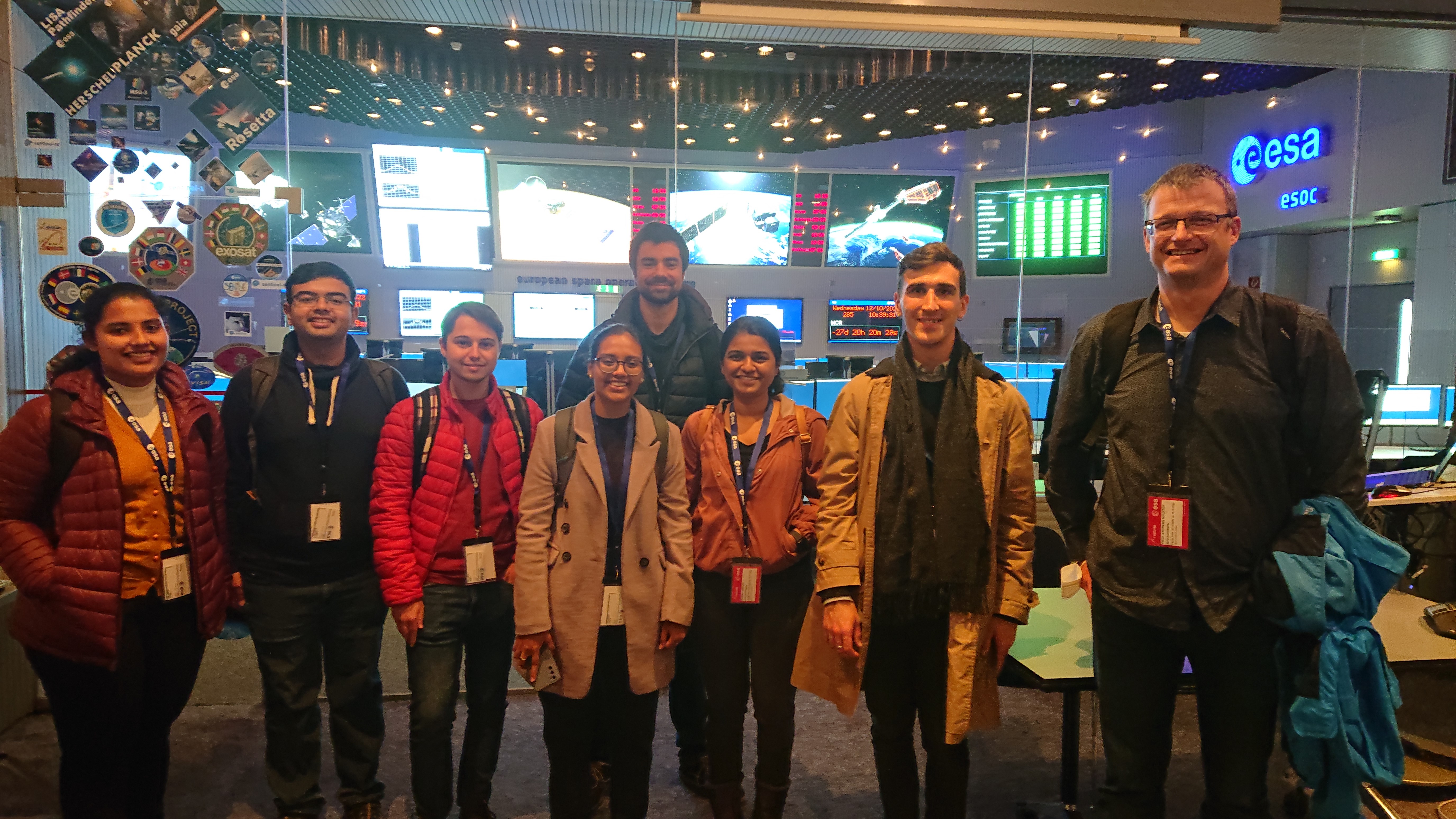 Eight people in front of a glass pane, behind which the main control room of ESA is located.