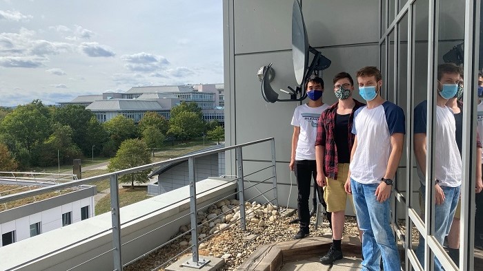 Three students stand in front of the parabolic antenna used to receive transmissions from the Es'hail 2 / QO-100.