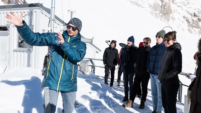 Mehrere Promovierende stehen mit Dr. Till Rehm vor dem Schneefernerhaus, im Hintergrund die Zugspitze.