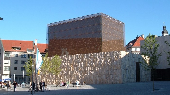 A building of stone and glass freestanding on a square.