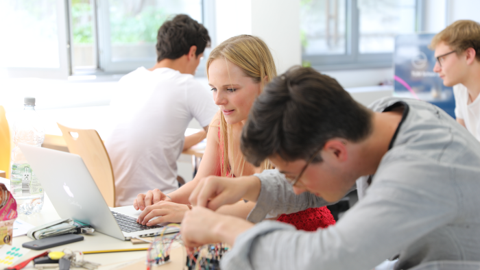  A young man and a young woman work on a computer and a circuit board.