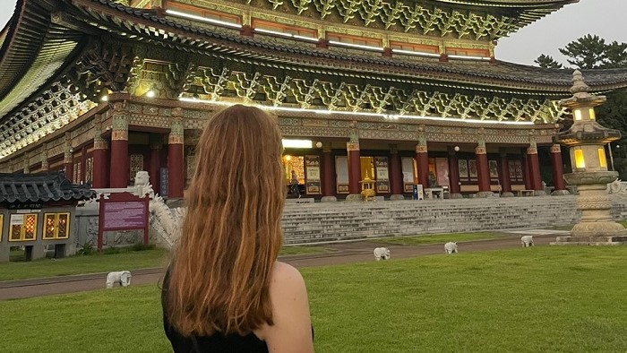 A young woman stands with her back to the viewer in front of a temple with a magnificent curved roof.