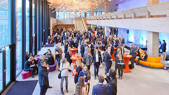 © Florian Freund There are many people standing in a large foyer talking to each other.