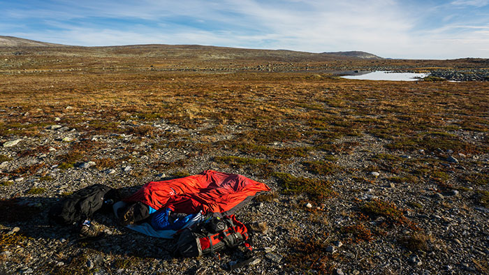 In einer weitläufigen, recht kargen Landschaft liegen zwei Trekking-Rucksäcke und zwei ausgerollte Schlafsäcke.
