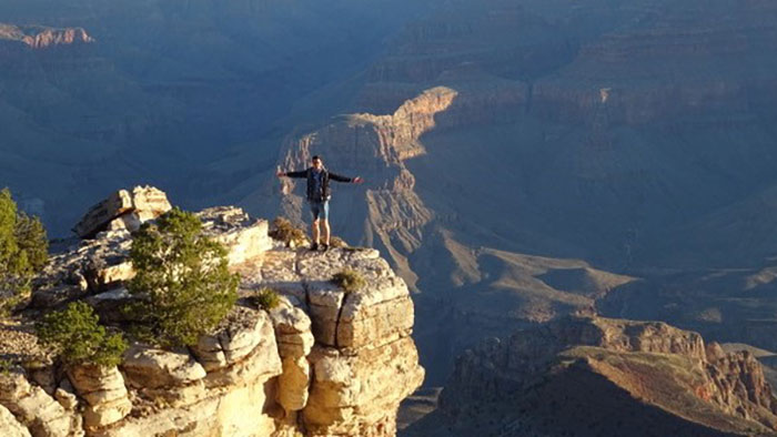 Panoramic landscape: a young man stands with his arms outstretched at the edge of a canyon.