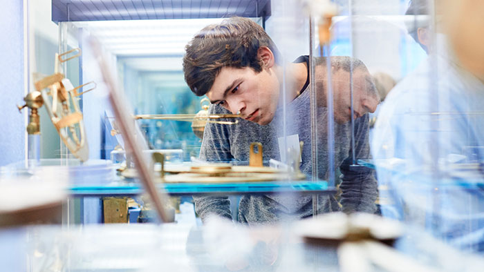 Ein junger Mann blickt interessiert und konzentriert durch eine Glasvitrine auf ein Ausstellungsstück.