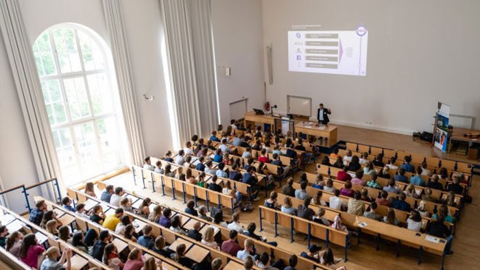 A crowd of people sit in a lecture theatre and listen attentively to a speaker.