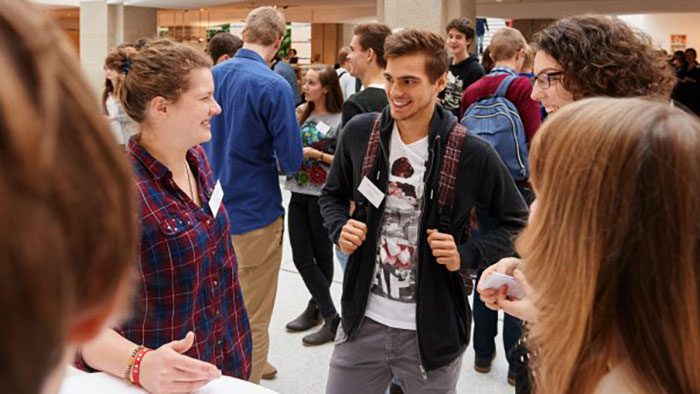 A group of young people at a reception stand by a table, smiling and chatting.