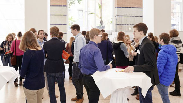 A large group of young people stand and converse in small groups.