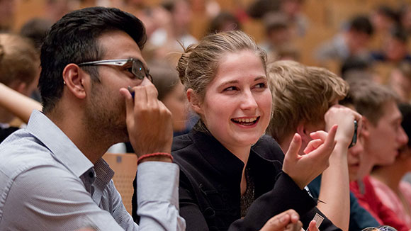 A young man and a young woman talking to each other in a lecture hall.