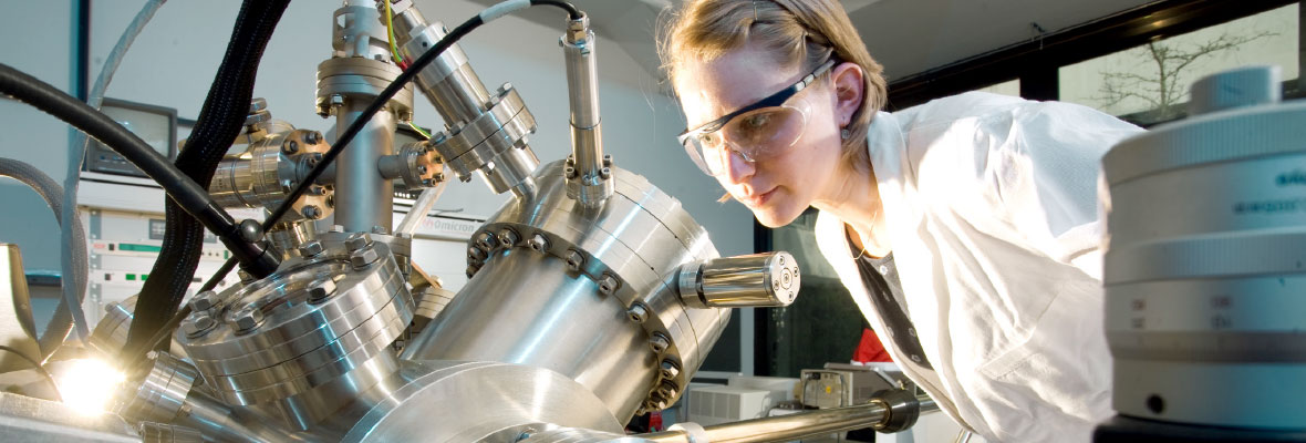 A young woman in a laboratory uses a piece of equipment to examine an object. 