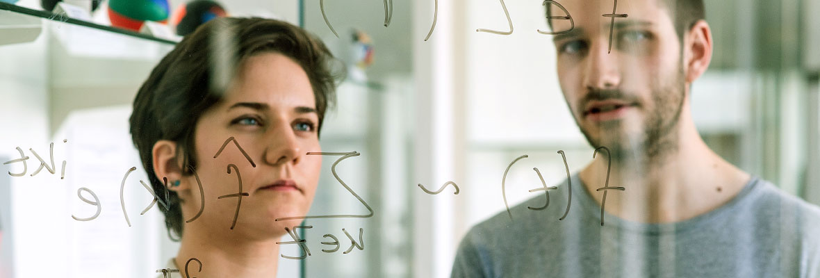 A woman and a man look at a scientific formula written on a board.