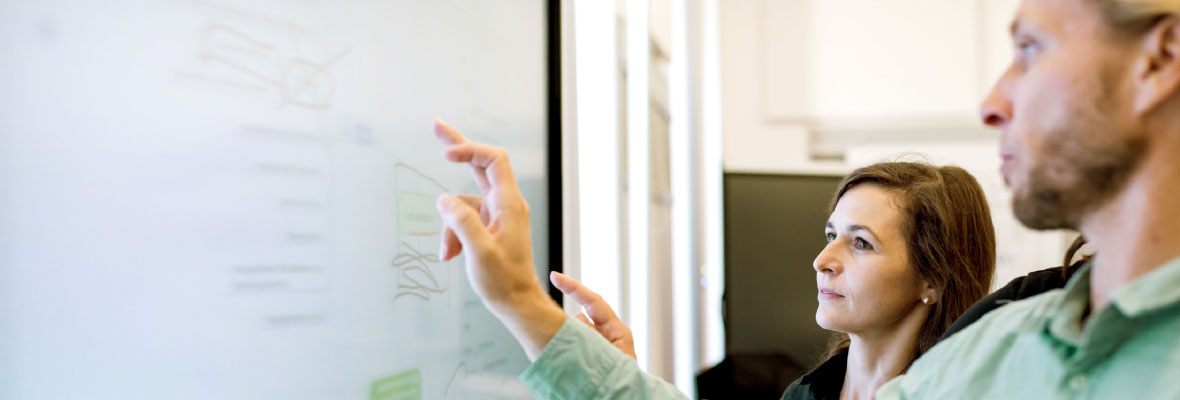 A man and a woman discuss formulas written on a whiteboard.