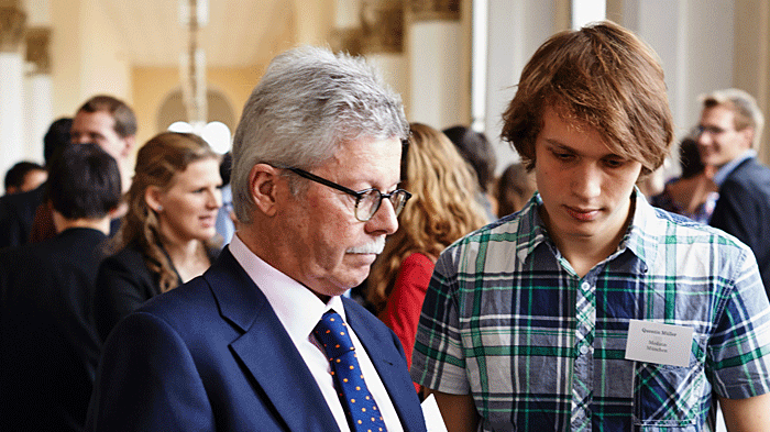 An older man explains an obscured document to a young man during an event.