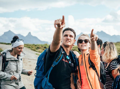 Zwei junge Menschen mit Wanderausrüstung zeigen auf etwas außerhalb des Bildes.