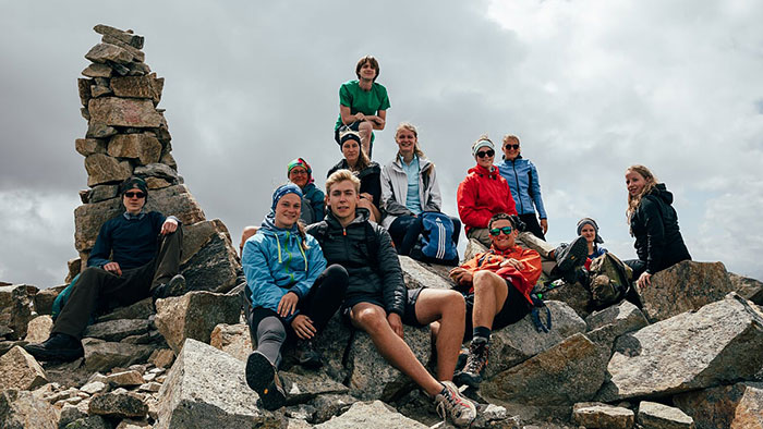 A group of young people rest happily on the summit of a mountain.