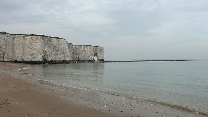 Landschaftsbild: Im Vordergrund des Bildes befindet sich ein Strand, der im Hintergrund des Bildes eine Steilküste zeigt.