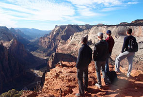 Three young people stand at the edge of a canyon and look into the distance.