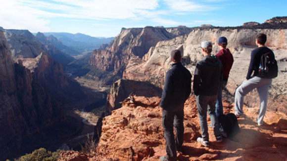 Several young people stand at the edge of a deep canyon and look into the distance.