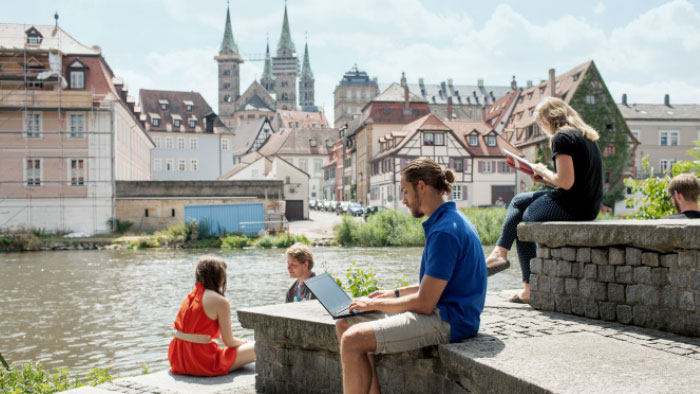 Junge Menschen sitzen auf Steinstufen an einem Fluss und lernen.