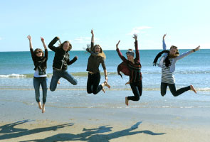 Photo of numerous students at a beach, leaping into the air.