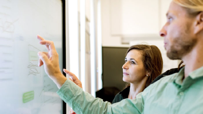 A man and a woman discuss formulae written on a whiteboard.