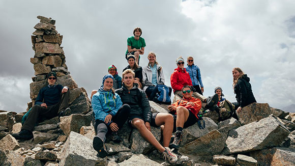 A group of young people rest happily on the summit of a mountain.