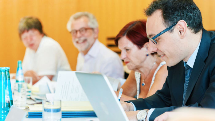 Members of a committee listen attentively and take notes.